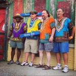 Four men wearing colorful shirts pose for a photo.