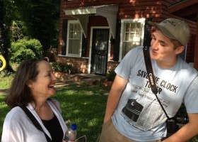 Two people outside a red house with a swing set.