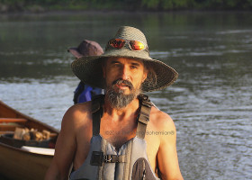 Man in a wide-brimmed hat by a canoe.