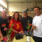 Four people smiling, holding drinks and flowers.