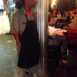 Man in hat and apron standing in a restaurant.