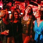 Three women smiling in a dimly lit bar.