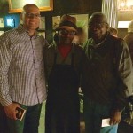 Three men standing together in a bar.