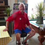 Man in red shirt smiles by a pool table.