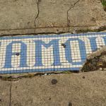 Tile mosaic spelling "FAMO" on sidewalk.