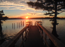 Wooden dock leading to sunset over lake.