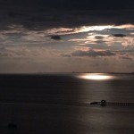 Pier and boat at sunset with cloudy sky.