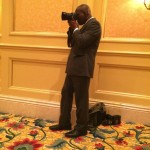 Man in suit taking a photo with camera.