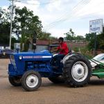 Man driving blue tractor with mower attachment.