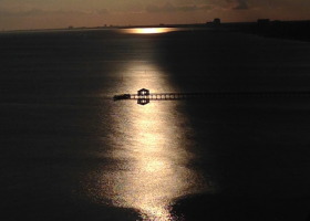 Silhouetted pier with sun reflecting on water.