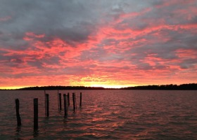 Pink and orange sunset over water with posts.