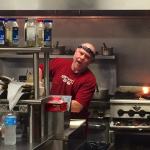 A man in a red shirt cooks on a griddle.