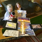 Two women and a dog pose with artwork.