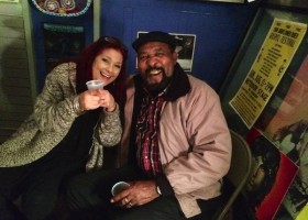 Two people smiling, holding cups, sitting together.