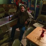 Man with beer sitting in a room with chairs