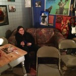 Woman sits on a couch in a room with chairs.