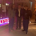 Three men standing outside an open store.