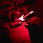 Man playing guitar in red lit room.