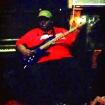 Man in red shirt playing bass guitar.