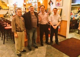 Four men smiling in a restaurant.