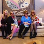 Four women pose on a white couch in a home.