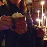 Woman holding a mug of hot cocoa by candlelight.