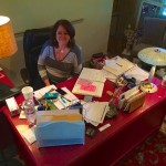 Woman sitting at a cluttered desk with a lamp.