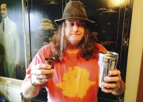 Man with hat holding a metal cup.