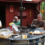 Three men enjoying snacks and drinks on patio.