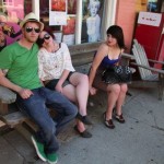 Three friends sitting on a bench outside a store.