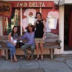 Three people sitting on a bench outside a store.