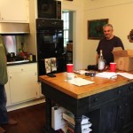 Two men in a kitchen with a table in front of them.