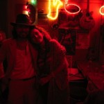 Two people pose for a photo in a red lit room.