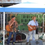 Two men playing guitars under a canopy.