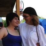 Two women, one holding a lens cap, smiling.