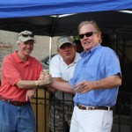 Three men smiling under a tent.