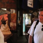 Two men, one wearing a cap, in a bar.