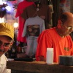 Man with yellow hat smiles at camera next to man.