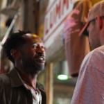 Two men talking, one wearing a brown jacket.