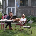 Two women sitting outside a wooden house.