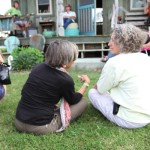 Two women sitting on grass with green foliage.