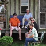 Four people sitting on a porch with a drink.