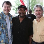 Three men smiling, one in a patterned shirt.