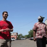 Two men standing on a street with cars.