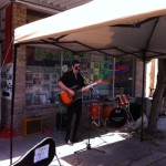 Man playing guitar with band under awning.