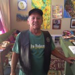 Man in green shirt and leather vest, art on the walls.