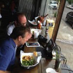 Two men eating at a table with drinks.