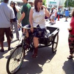 Woman in a white shirt riding a bicycle cart.