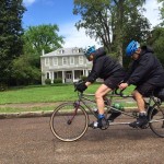 Couple riding a tandem bicycle on a street.