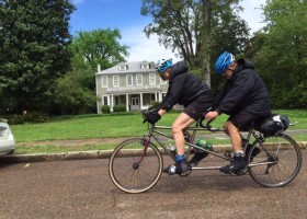 Couple riding a tandem bicycle on a street.